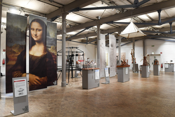 In einem Ausstellungsraum stehen Exponate auf Sockeln, im Hintergrund hängt ein großes Plakat der Mona Lisa