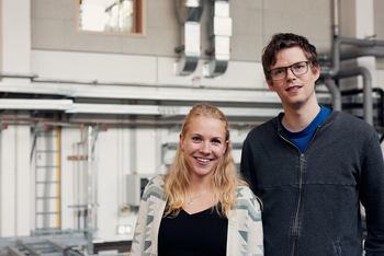 Doppelporträt von Tessa Strümpfler und Thomas Zimmermann die versetzt nebeneinander in der Experimentierhalle der HSBI stehen und lächelnd in die Kamera