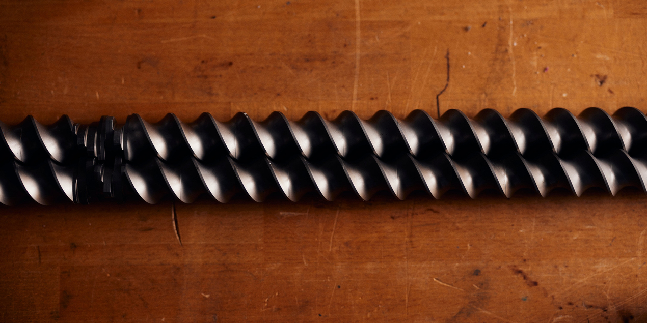 Detailaufnahme der beiden spiralförmigen Rührstäbe des Doppelschneckenextruders Die beiden Metallstäbe sind circa einen Meter lang und liegen auf einer dunklen Tischplatte aus Holz